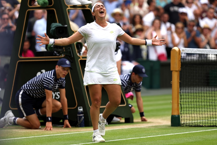 A tennis player stands with her arms outstretched in celebration.