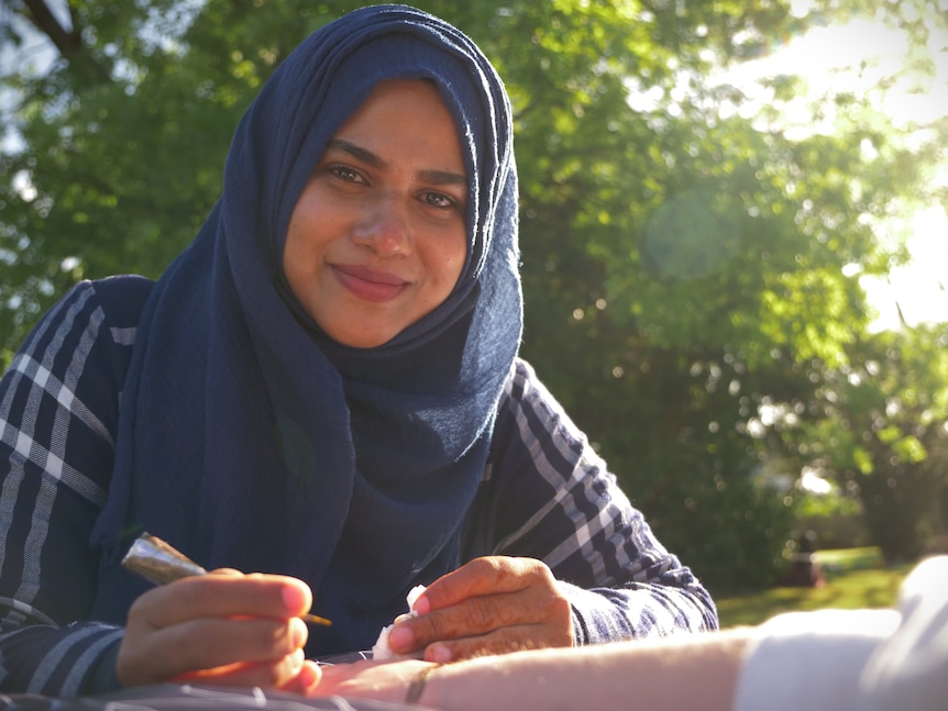 A woman in a hijab smiling to camera and holding a henna cone