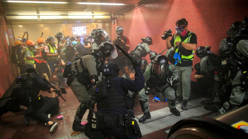 In a subway station, police swarm protesters and beat them with batons in front of escalators.
