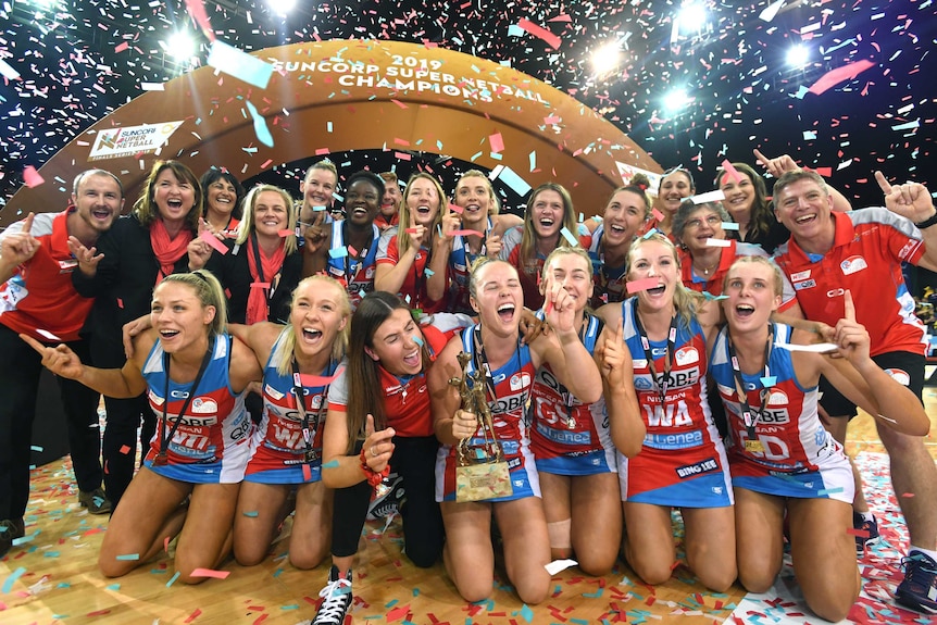 NSW Swifts players smile for a victory photo with a gold trophy