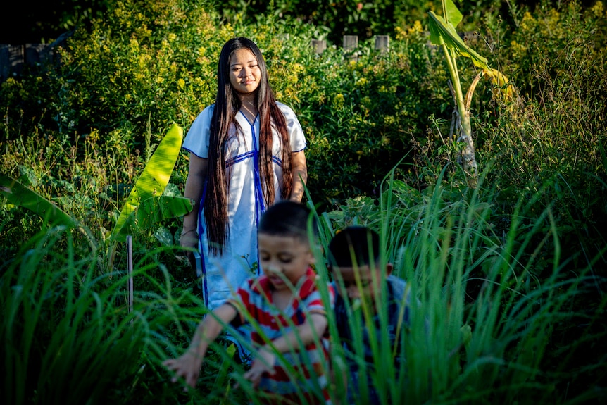 Woman smiles in garden as two small boys play nearby. 