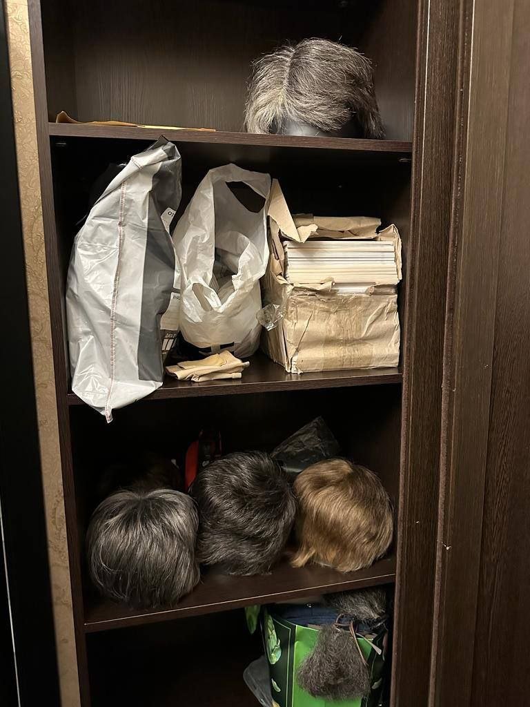 A set of shelves with papers and a collection of wigs laid out on them.