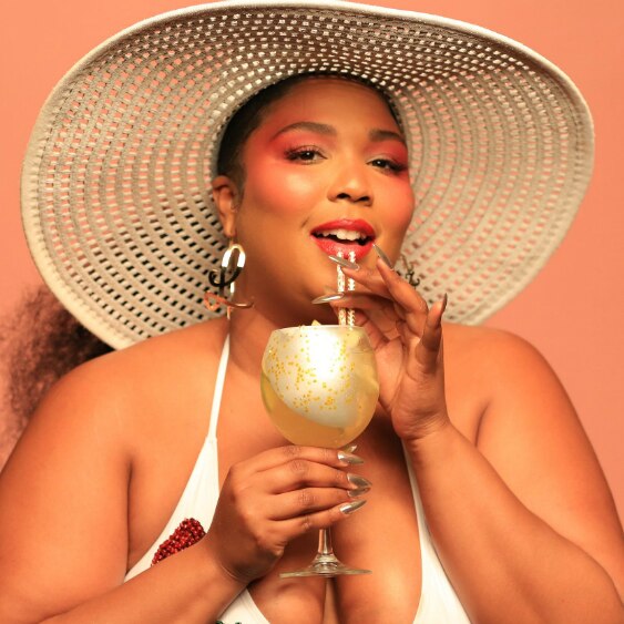 Lizzo wears a sun hat and sips on a drink through a straw