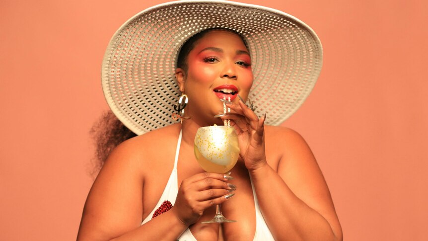 Lizzo wears a sun hat and sips on a drink through a straw