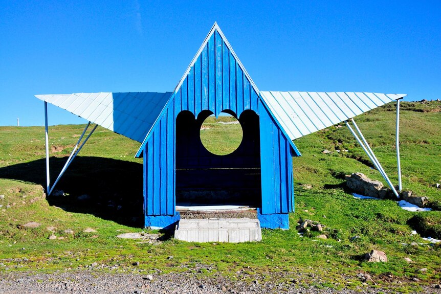 A blue bus stop with a pointed high roof