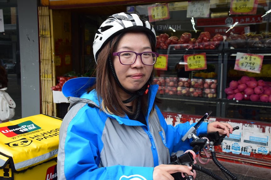 Una mujer sentada en una bicicleta de reparto de comida.