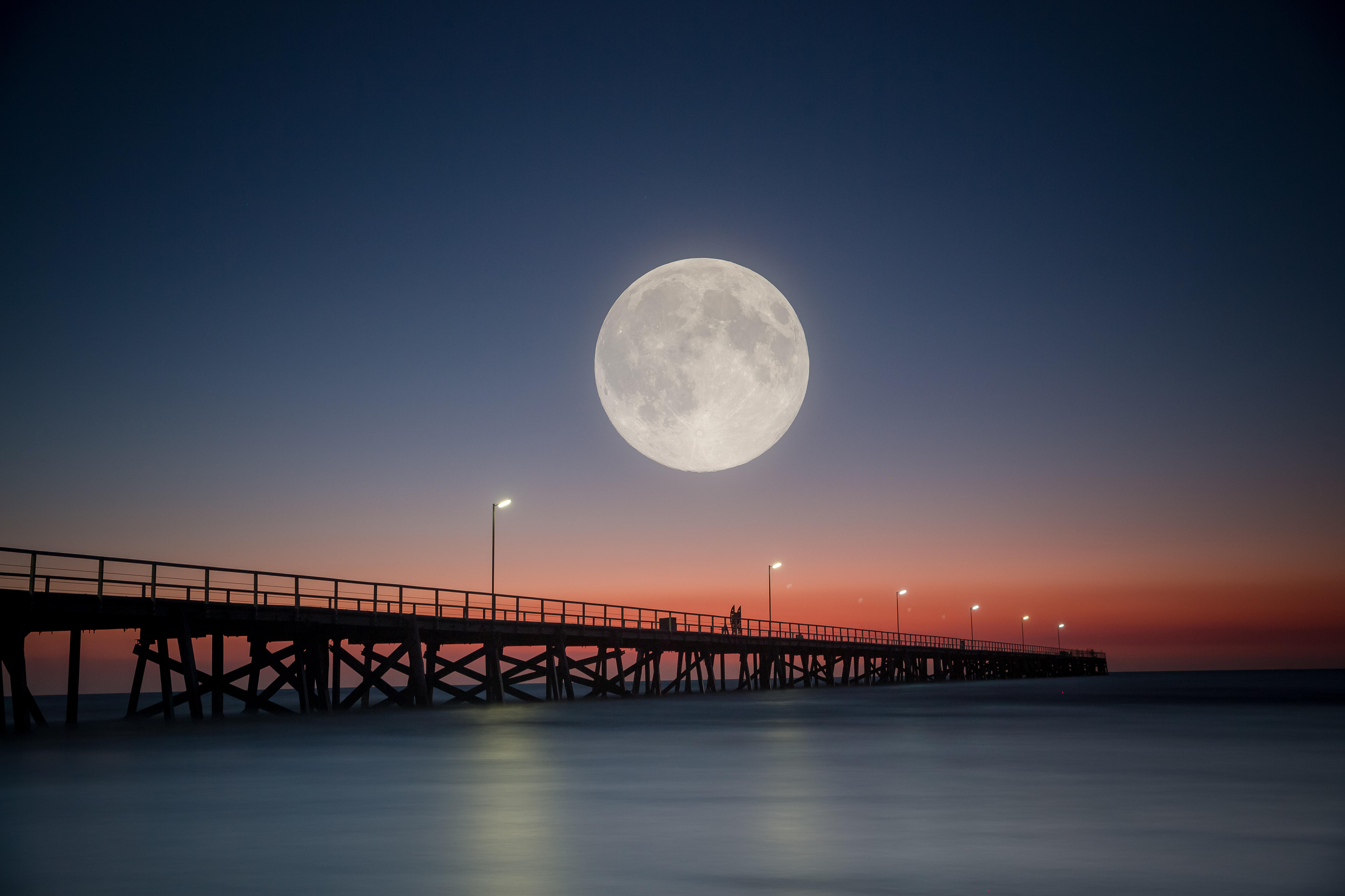 A large white moon just above a jetty at sunset