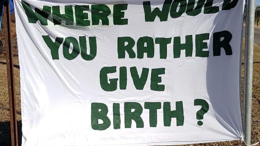 A banner is tied up to two poles that reads " Where would you rather give birth?"