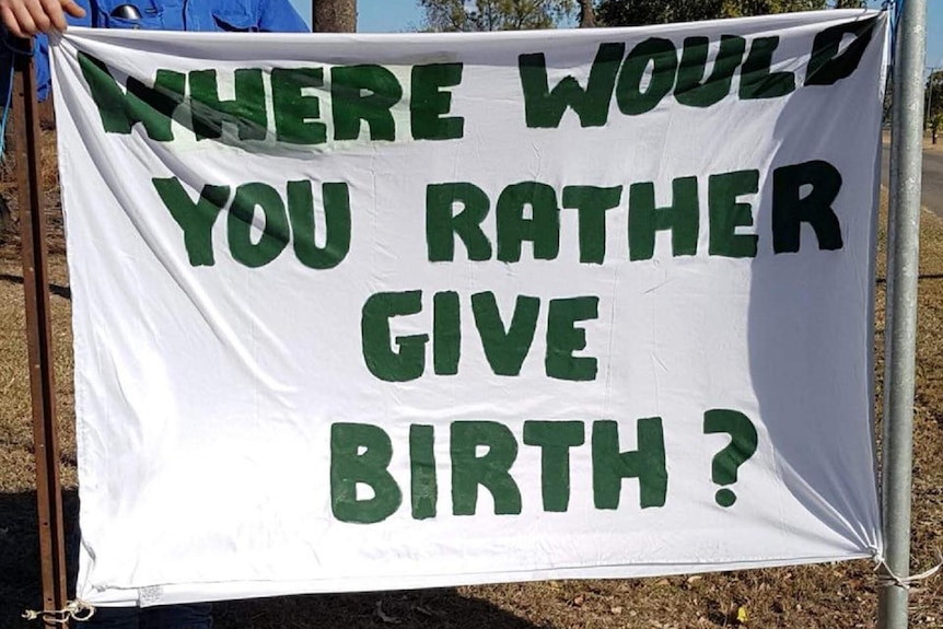 A banner is tied up to two poles that reads " Where would you rather give birth?"