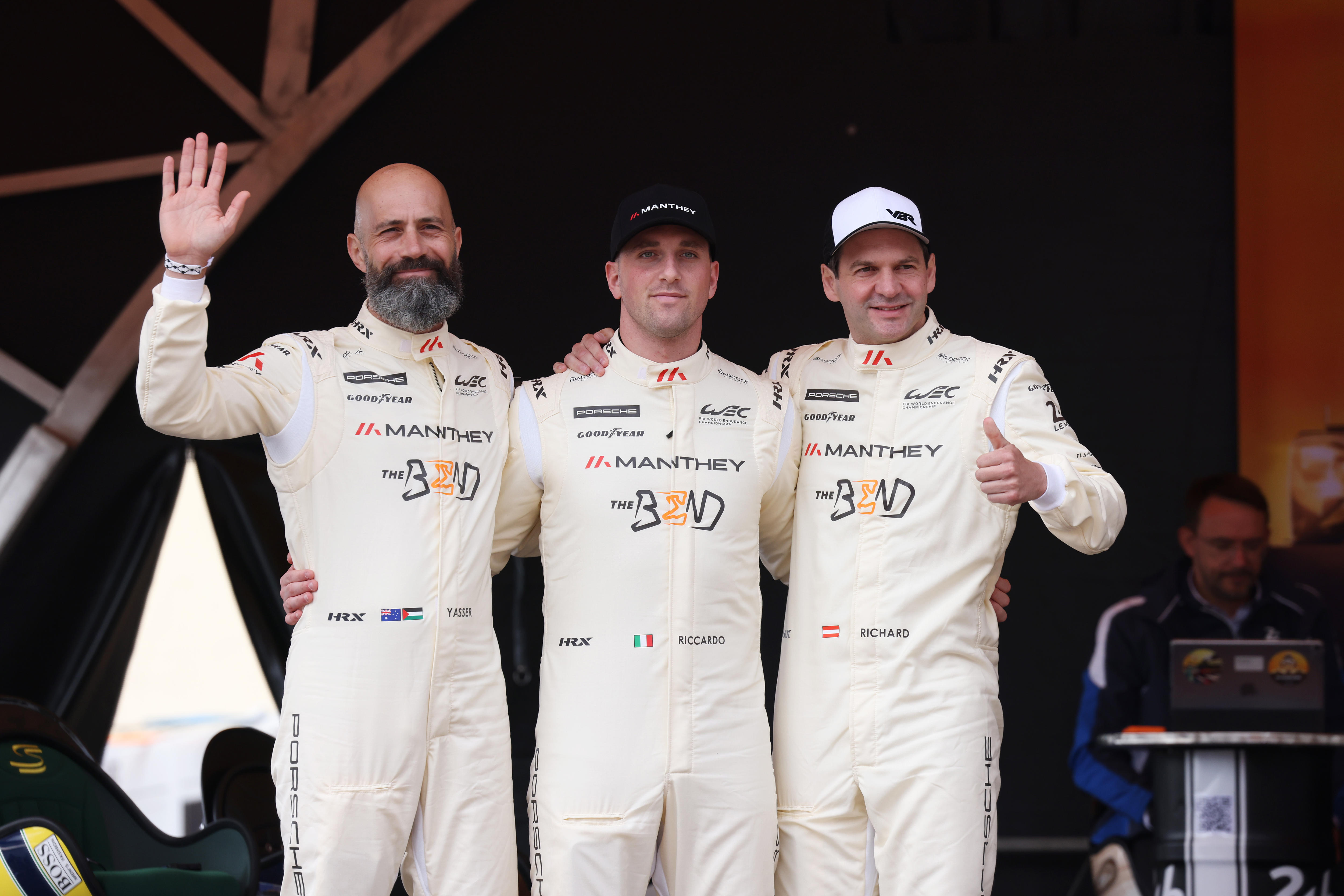 Three racing drivers, arm in arm, waving to fans at an opening ceremony