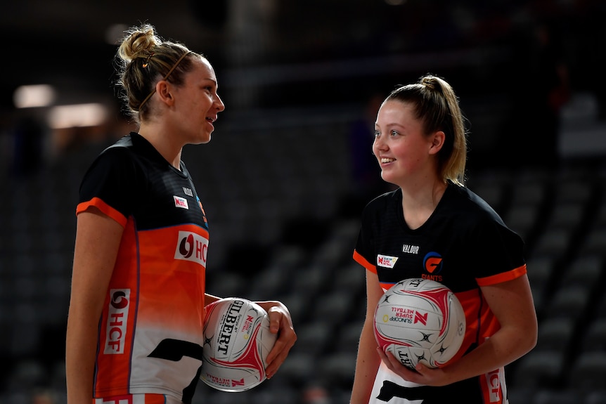 Two players smile at each other with balls in their hands as they warm up 