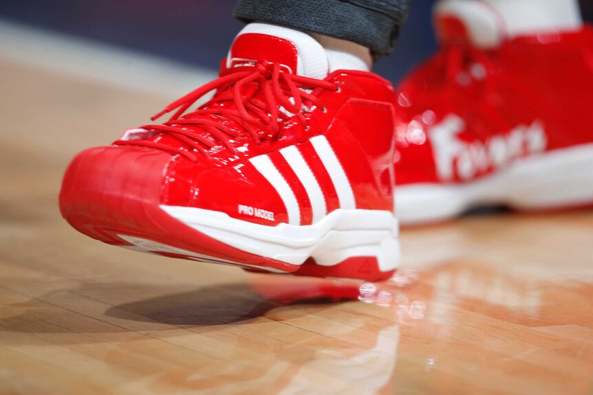 A close up of a pair of bright red shiny runners with three adidas stripes.