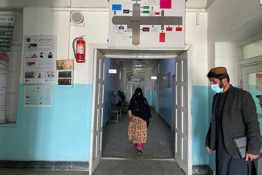 A woman in a head scarf walks through the entrance of a hospital with blue walls