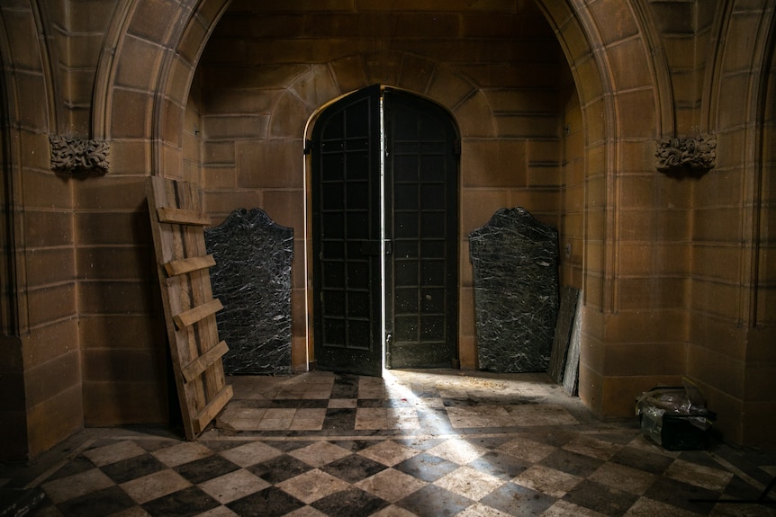The interior of a stone building with black and white tiles and large stone grave heads.