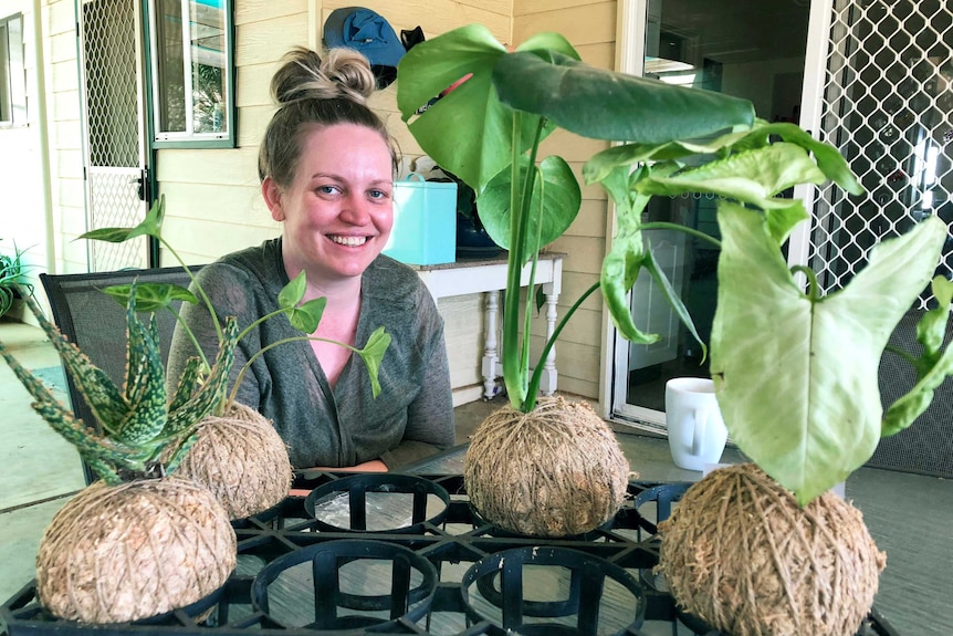 A woman sits on a verandah with kokedamas on an outdoor table.