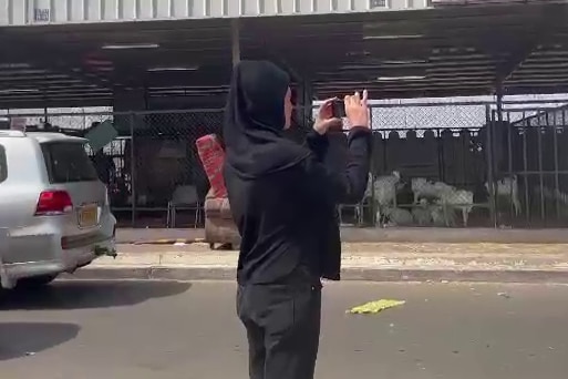 Woman wearing all black and in a hijab takes a photo outside a facility.