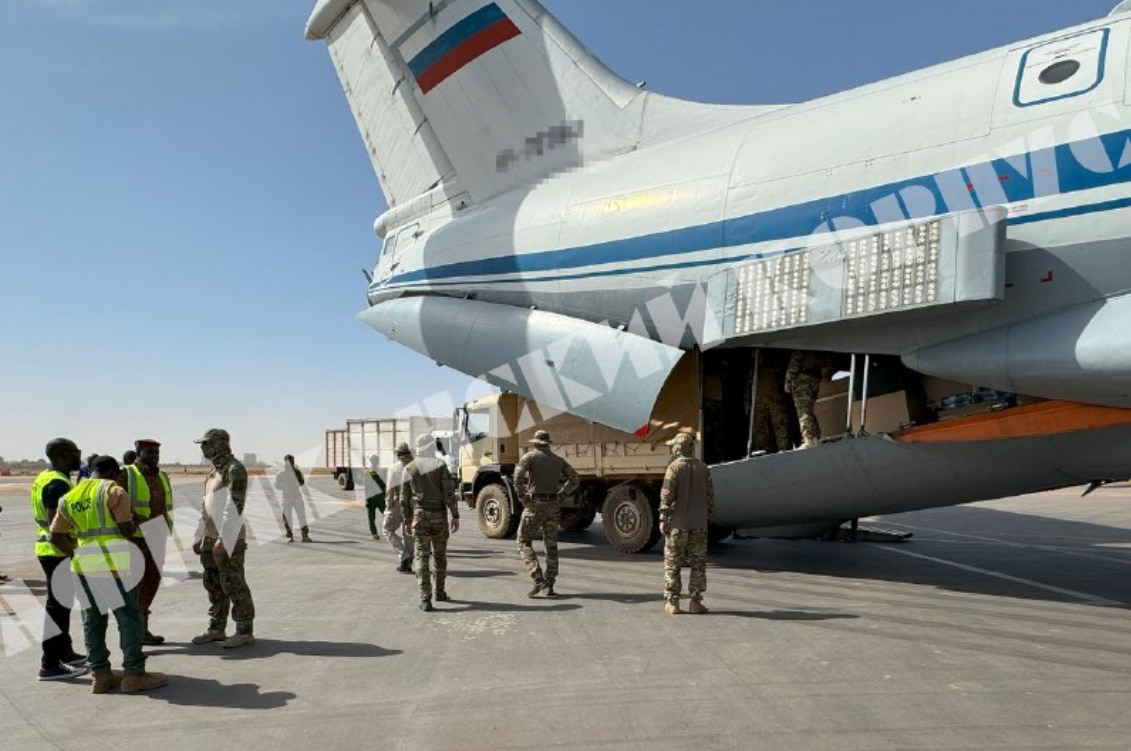 Military troops speaking with Africans on an airplane tarmac.
