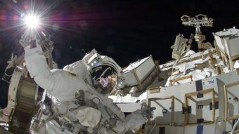 Sunita Williams is seen in a space suit with a spaceship behind her, and the black expanse of space above her.