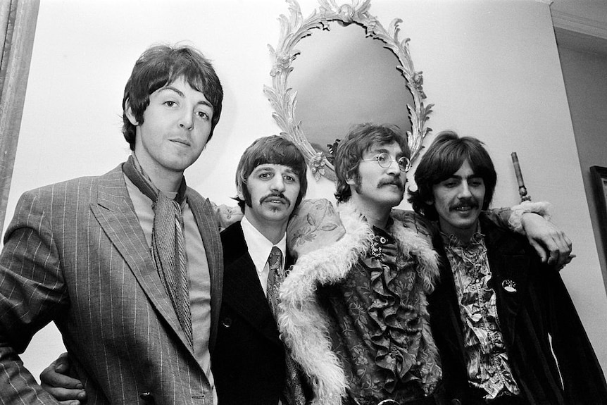 The Beatles stand with arms around each other's shoulders.