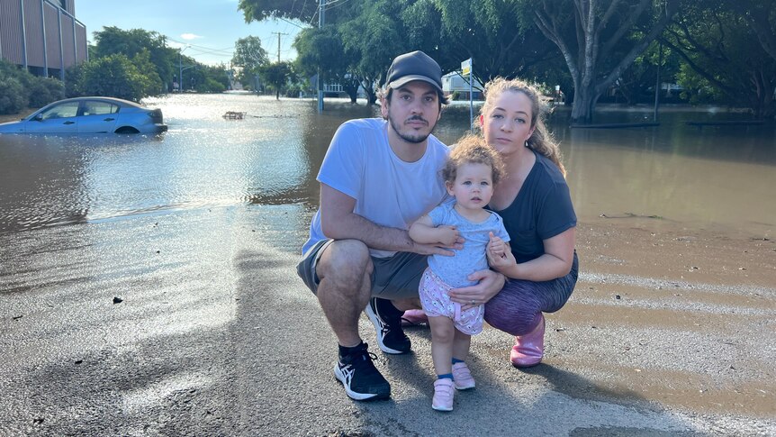 A child with parents with a submerged car in the background.