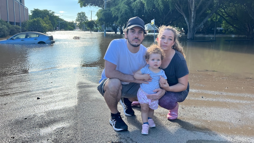 A child with parents with a submerged car in the background.