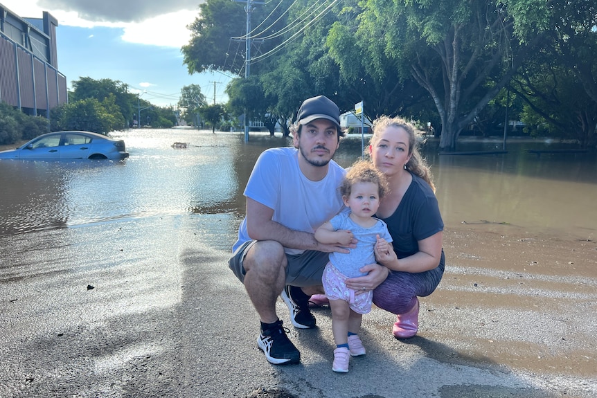 A child with parents with a submerged car in the background.