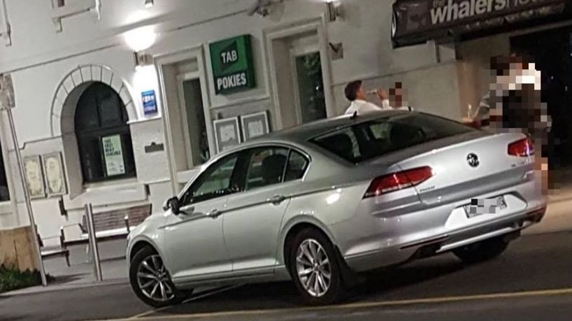 A man stands next two a car and has a beer, unaware that his photo is being taken.