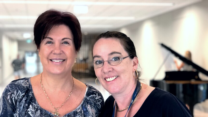 Two women standing in front of piano, smiling.