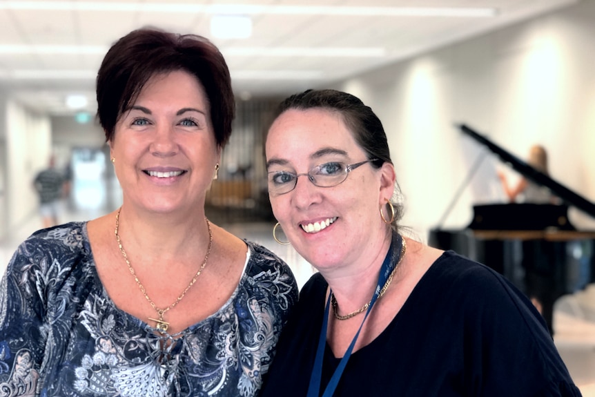 Two women standing in front of piano, smiling.