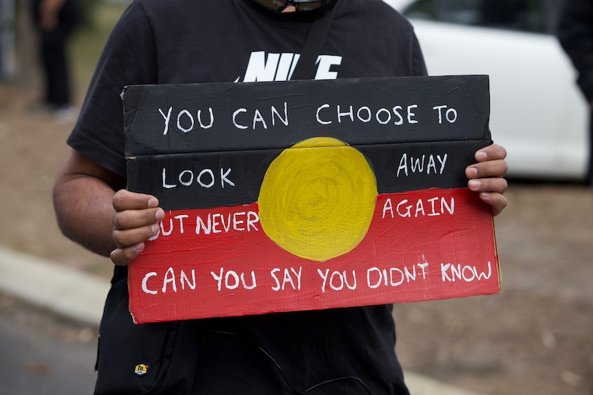 An Indigenous person holding a sign saying the government is not looking after youth detainees