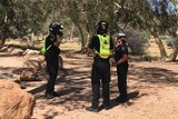 Three police officers stand near each other on red dirt near gum trees