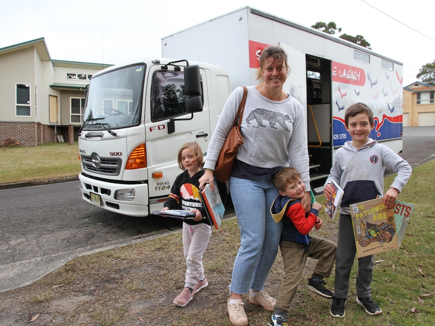 A woman with three small children pose near the bookmobile truck for a photograph