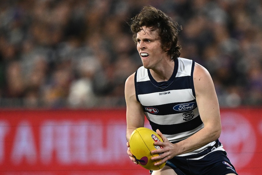 A Geelong AFL player holds the ball in both hands during a match.