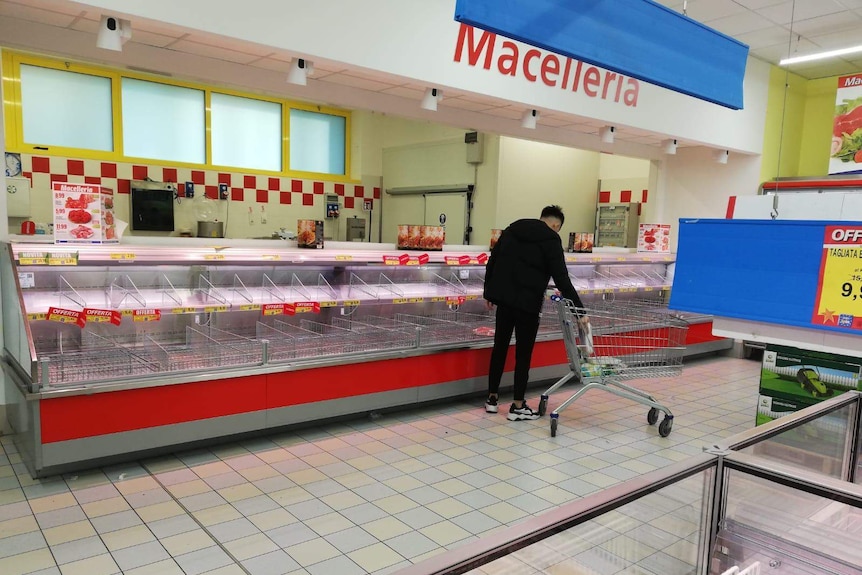 A man with a trolley places some items in it beside a near-empty aisle.