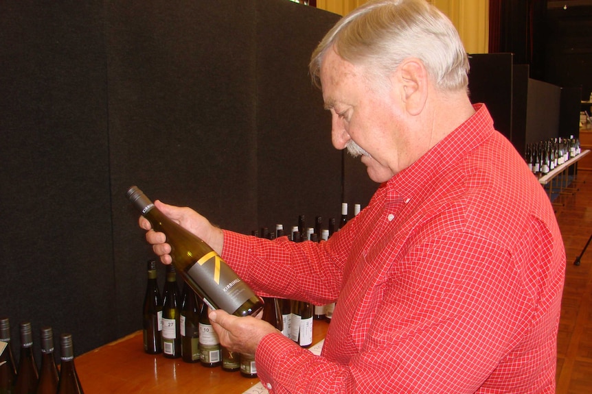 Wine judge Jim Tresize holds and inspects a bottle of wine.