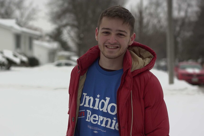 A young man standing on a snowy street in Iowa in a Bernie t-shirt