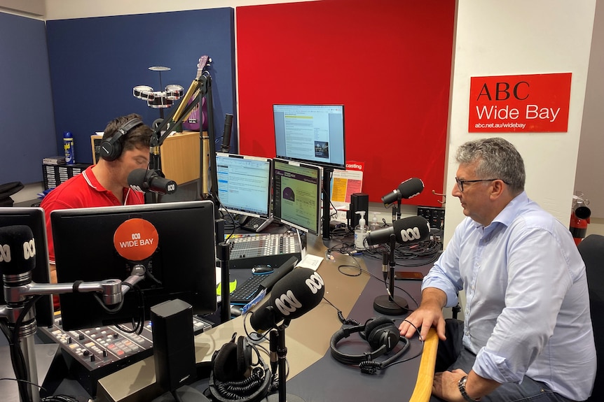 Two man sit across from each other in a radio booth doing an interview