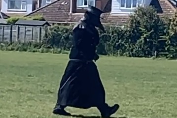 A person walking dressed in long black cloak, hat and beak-shaped mask.