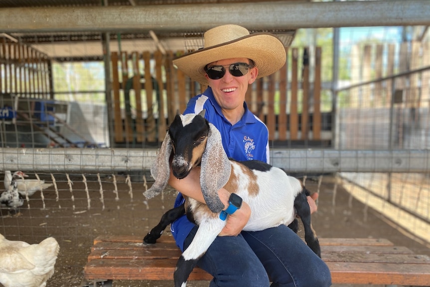 Man smiling and holding a goat on a farm