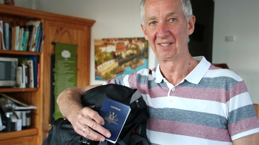 A man in a striped shirt holds up a backpack and passport.
