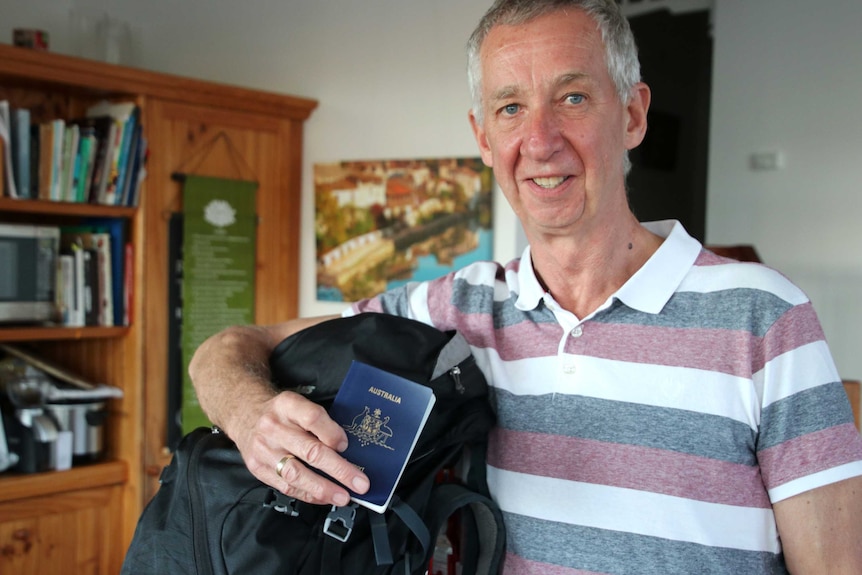 A man in a striped shirt holds up a backpack and passport.