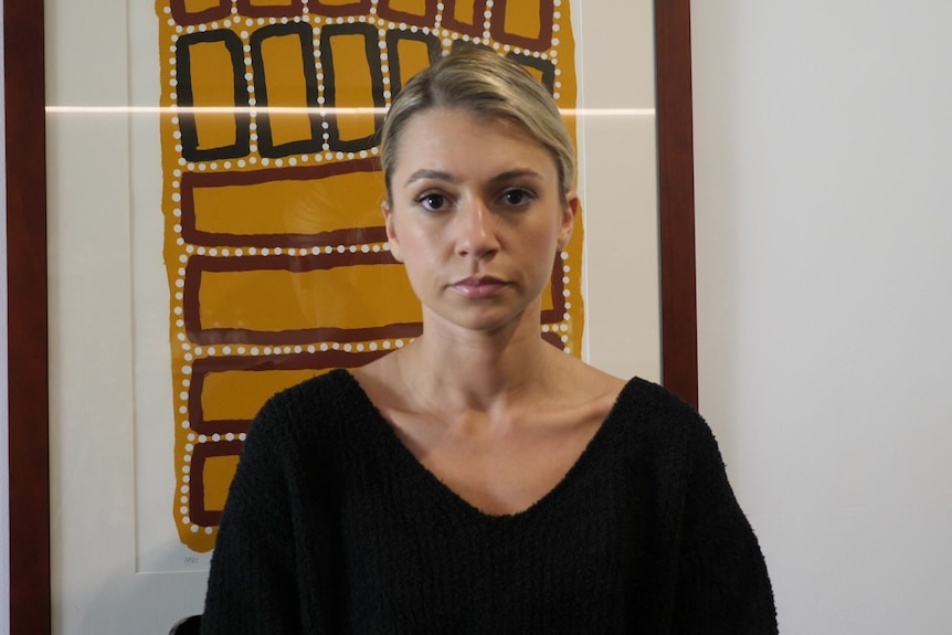 Jade Torres in front of Aboriginal artwork. Her expression is neutral