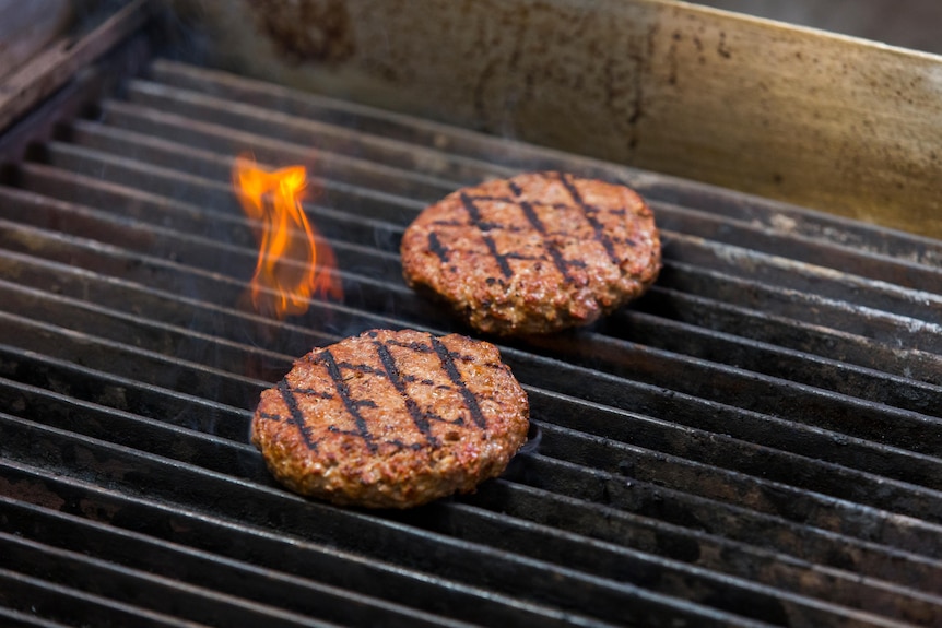 Fake meat burgers cooking on a grill.