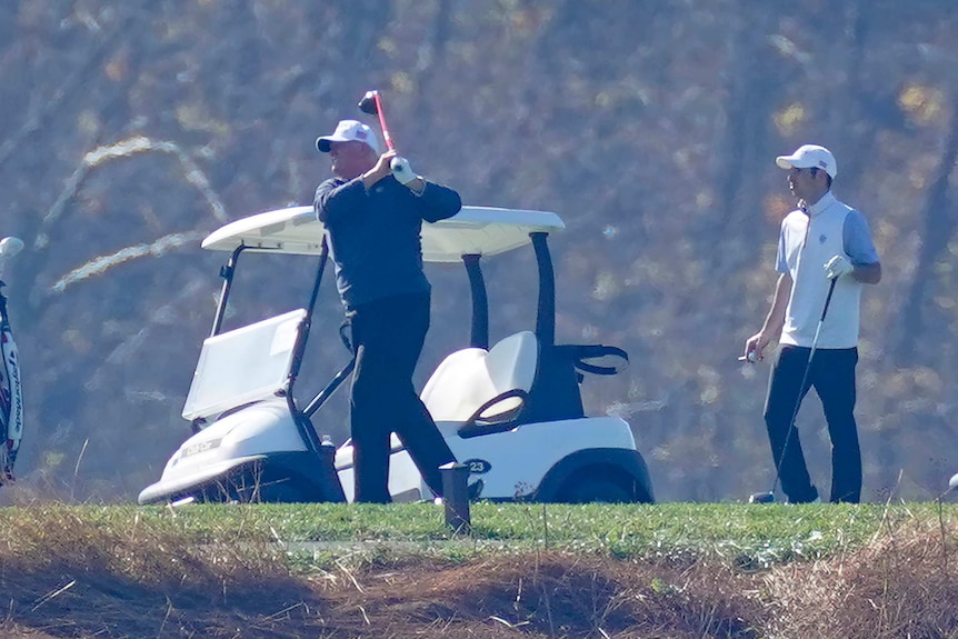 Trump swings a golf club, alongside a caddy