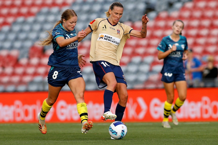 A Newcastle Jets A-League Women player dribbles the ball as she is challenged by a Wellington Phoenix opponent.