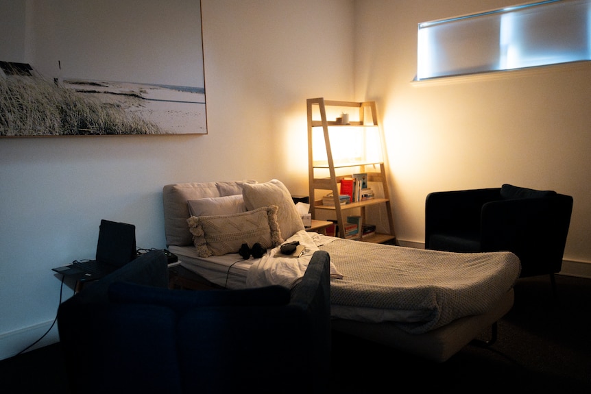 A dimly lit room with a bed and two couches next to it, with a pair of headphones on the bed.