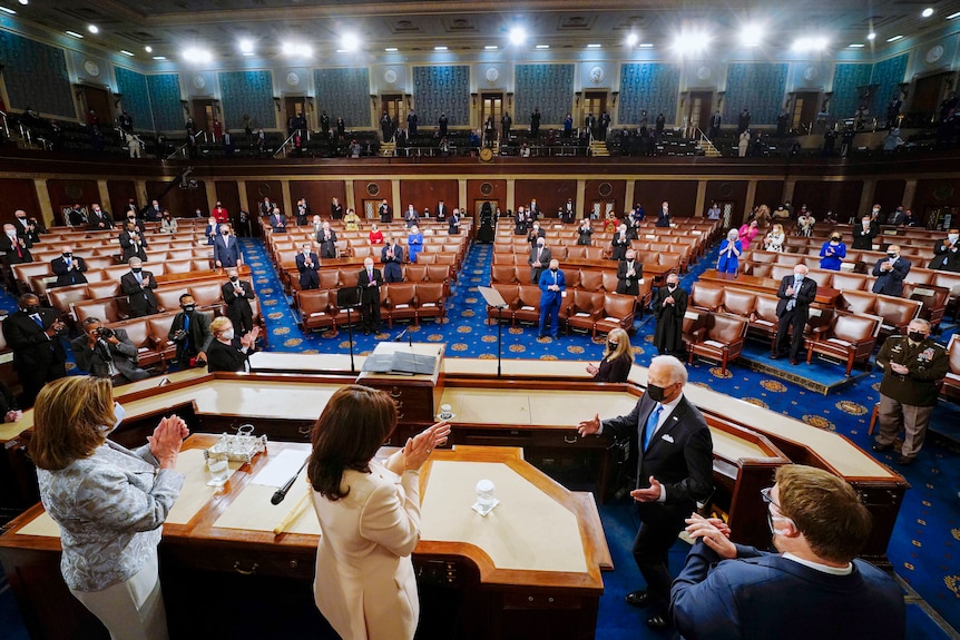 Joe Biden in a face mask gestures to Kamala Harris in the US House chamber in front of a small crowd