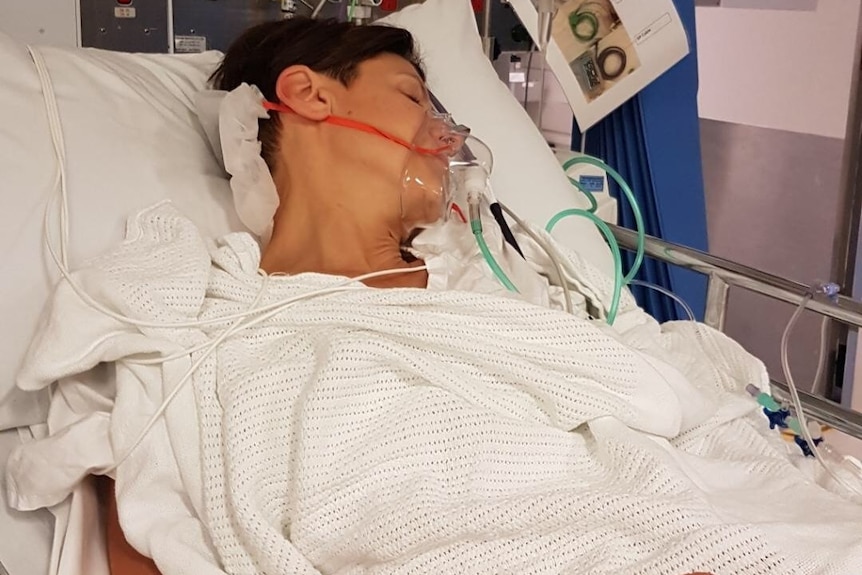Emma Alberici laying in a hospital bed, she has a breathing mask on and is attached to a drip.
