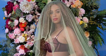 Beyonce caresses her pregnant belly while wearing a veil in front of a floral arrangement