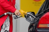 A woman uses a fuel dispenser to fill her car up with petrol at a petrol station.